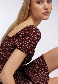 Abito bordeaux floreale con maniche corte a sbuffo, tessuto testurizzato e corpetto aderente. La gonna presenta una leggera svasatura e piccoli motivi floreali chiari.