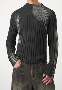 Mörkgrå ribbad tröja med hög krage och detaljer med dragkedja. Har långa ärmar med lätt frans vid kanten och texturerad tyg.