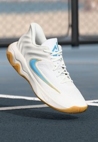 Witte sportieve schoen met gestructureerde stof, lichtblauwe accenten en een gum zool. Heeft een rond ontwerp en vetersluiting.
