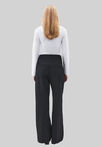 Donkere grijze pinstripe broeken met wijde pijpen, een hoge taille en achterzakken, gecombineerd met een nauwsluitend wit langermig shirt.