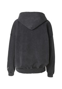 Sort oversized hettegenser laget av mykt stoff, med hette, ribbet midje og mansjetter, og en liten pynt på venstre erme.