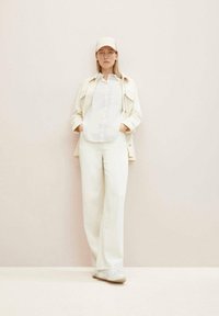 O ținută casual de culoare deschisă, compusă dintr-o cămașă cu nasturi, pantaloni cu croială relaxată, o jachetă ușoară și o șapcă asortată.