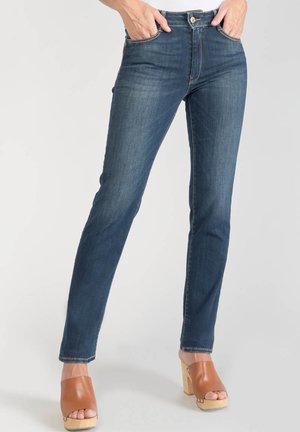 Jean skinny en denim bleu foncé avec un design ajusté, cinq poches et des coutures contrastantes. Associé à des sandales à plateforme marron.