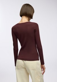 Burgundowa bluzka z długim rękawem, z okrągłym dekoltem i dopasowanym krojem. Gładka tekstura w połączeniu z jasnymi, luźnymi spodniami.
