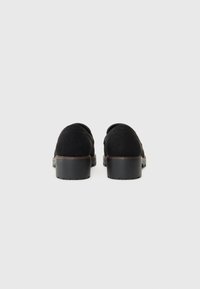 Zapatos de ante negros con un tacón bajo en bloque, que presentan una textura suave y un diseño redondeado. La parte trasera muestra sutiles detalles de costura.