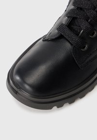 Botte en cuir noir avec bout arrondi, lacets épais noirs et semelle en caoutchouc robuste sur fond blanc uni.