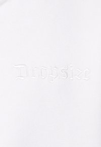 Bijela pamučna majica s izvezenim tekstom "Dropsize" u stiliziranom fontu, suptilnom teksturom i bez dodatnih grafika ili uzoraka.