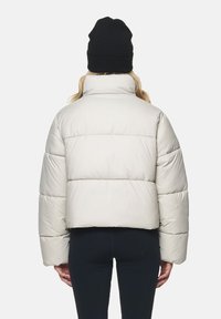 Gekürzte, hellbeige Daunenjacke mit hohem Kragen und gesteppten Abschnitten. Getragen mit einer schwarzen Beanie, zeigt die Rückansicht ein elegantes Design.