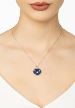 Silver necklace featuring a round pendant with a deep blue background and white star pattern, resting on a smooth, bare neck.