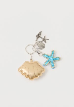 Llavero con bolsa dorada en forma de concha, estrella de mar azul con cuentas y tres pequeños colgantes plateados de conchas y estrella de mar sobre un fondo blanco.