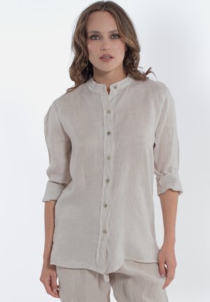 Chemise en lin beige clair avec un col montant, manches longues retroussées et fermeture centrale à boutons avec des boutons de couleur verdâtre.