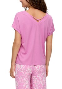 Lichtroze top met korte mouwen en een V-vormige achterkant met gekruiste bandjes. Zacht fabric en een relaxte pasvorm. Draag het met bloemenpatroon roze broek.