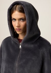 Abrigo con capucha de un gris oscuro, hecho de un tejido suave y esponjoso, que presenta un cierre de cremallera y una capucha redondeada. Diseño minimalista, sin patrones.