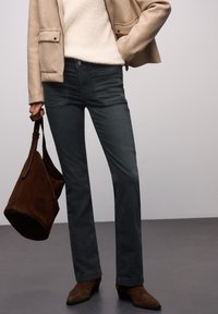 Vaqueros de pierna recta de color gris oscuro con textura ligera y bolsillos sutiles, combinados con un suéter crema y un bolso de ante marrón.