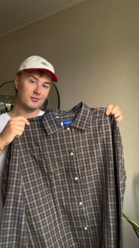 Camicia a maniche lunghe a scacchi marroni e bianchi con colletto a punta, chiusura a bottoni e due tasche sul petto. Tessuto morbido con una texture liscia.