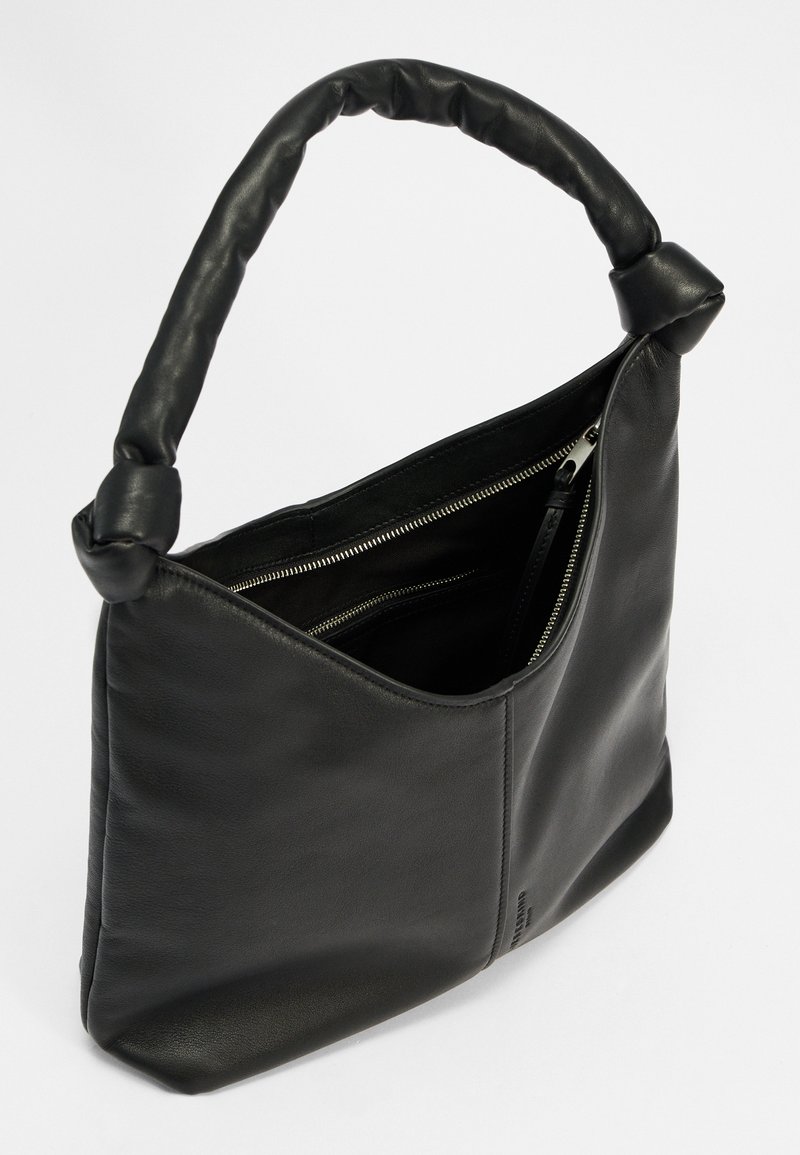 Schwarze Lederhandtasche mit einem geknoteten Griff, schickem Design und einem Reißverschlussfach innen. Weiche Textur und kantige Form mit minimalen Akzenten.