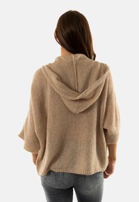 Pull à capuche tricoté de couleur marron clair avec des manches larges et une coupe décontractée. Tissu texturé avec une maille légèrement ouverte.