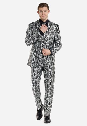 Completo stampato in bianco e nero con design aderente. La texture imita le squame di un serpente, indossato con una camicia nera e scarpe coordinate.