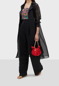 Musta läpikuultava pitkä paita, värikäs kuviollinen toppi, mustat leveälahkeiset housut ja punainen teksturoitu käsilaukku kullalla varustetulla kahvalla ja yksityiskohdilla. Kulta sandaalit.