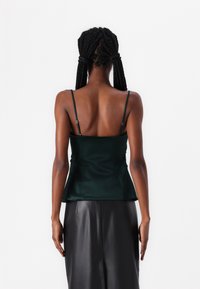 Green satin camisole with thin adjustable straps, featuring a fitted bodice and a flared hem, paired with a black leather skirt.
