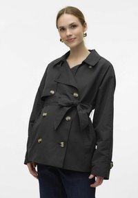 Svart trenchcoat med dubbelknäppt design, stora knappar, långa ärmar och ett knytbart midjebälte. Slät textil och klassisk krage.