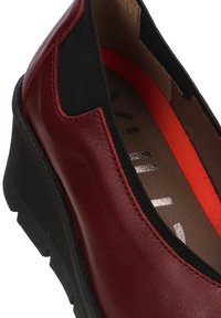 Zapato burdeos sin cordones con parte superior de cuero, paneles laterales elásticos, suela de goma negra texturizada y acento rojo en la plantilla.
