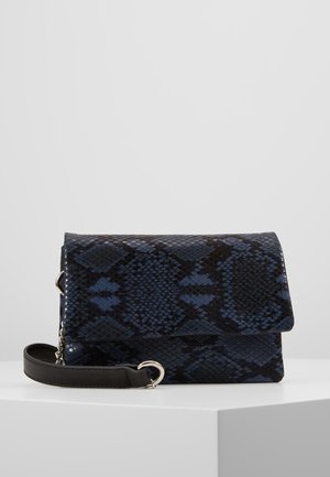 Compacte donkerblauwe en zwarte clutch met slangenhuidpatroon, met een afneembare zwarte leren polsriem en zilverkleurige hardware, rustend op een witte ondergrond.