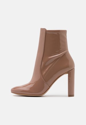 Bottine en cuir verni beige brillant avec talon bloc et bout pointu, finition lisse, détail de couture latérale, sur fond blanc.