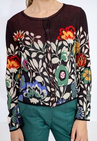 Cardigan en tricot présentant un motif floral aux couleurs vives sur un fond foncé, avec des boutons noirs et des manches longues.