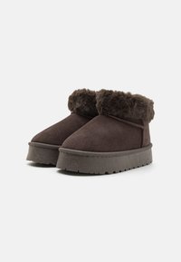 Bottines en suède marron avec doublure en fausse fourrure, bout arrondi et semelle en caoutchouc épaisse. Présente un design à découpe basse avec un détail de couture.