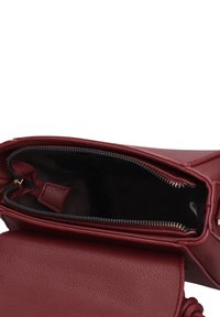 Borsa a mano in pelle color bordeaux con chiusura superiore con cerniera e finitura testurizzata. Interno con fodera scura e una piccola tasca. Dettagli discreti ai bordi.