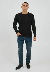 Pull en tricot côtelé noir avec un col rond, associé à un jean en denim bleu et des baskets noires, offrant un design ajusté.