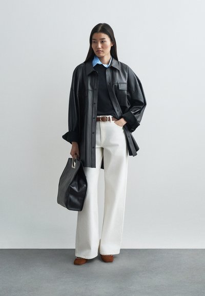 Black leather oversized shirt, navy sweater, white wide-leg trousers, brown shoes, and a black handbag with a silver accent.