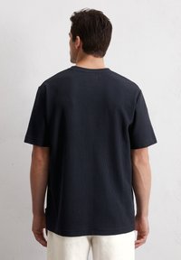 Granatowy t-shirt z krótkim rękawem wykonany z fakturowanej tkaniny, z okrągłym dekoltem. Posiada prosty krój i mały detal z logo w okolicy dołu.