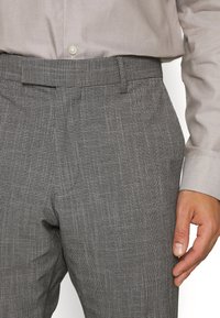Gray checkered trousers with a textured finish, featuring a flat front, belt loops, and a tailored fit, paired with a light-colored shirt.