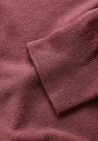 Tuvu plānoti violeta tamborēta džempera piedurknes daļa ar smalku ribotu tekstūru un auduma detaļām.