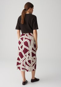 Pull en maille à manches courtes marron associé à une jupe bordeaux avec un motif abstrait crème, taille élastique et longueur mi-mollet.