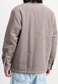Braune Cordjacke mit lockerer Passform, vertikal gerippter Struktur, langen Ärmeln und Seitenschlitzen am Saum.