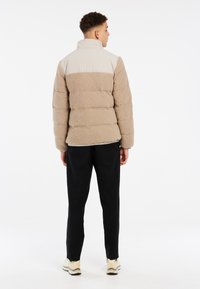 Doudoune beige et crème avec un matériau texturé et duveteux sur le corps et une partie supérieure lisse. Associée à un pantalon noir et des baskets légères.