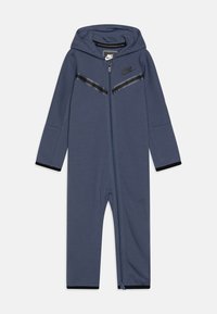 Un mono azul marino con cremallera y capucha, con acentos de rayas negras, puños elásticos y el logo de Nike en el pecho; fabricado con un material suave y elástico.