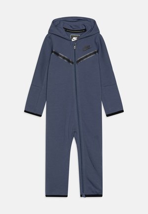 Une grenouillère zippée bleu marine avec capuche, ornée de accents en bande noire, de poignets élastiques et du logo Nike sur la poitrine ; fabriquée dans un matériau doux et extensible.