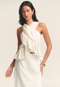 Haut blanc sans manches avec un design croisé et un ourlet froncé. Fabriqué en tissu léger, il présente une texture douce et une silhouette fluide.