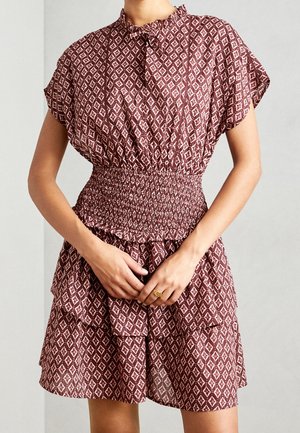 Sukienka w czerwono-kremowy wzór z krótkimi rękawami, marszczoną talią i falbanowym dołem. Wykonana z lekkiego materiału, z kołnierzykiem.