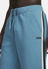 Lichtblauwe sweatpants van zachte stof, met een zwart-wit zijstrook, een verstelbare tailleband en een klein logo label.