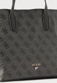 Svart totebag med teksturert mønster, glatte detaljer og gulllogo. Designet inkluderer to håndtak og en strukturert form.