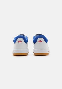 Bílé tenisky s modrými síťovinovými límci, gumovými podrážkami a červenými logy krokodýla na patě, vyobrazené zezadu na bílém pozadí.