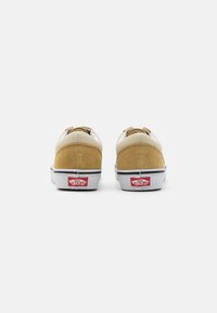 Zapatillas de ante marrón y cuero crema con suelas blancas, que presentan un logo de Vans en rojo y negro en el talón. Suela de goma para mayor tracción.