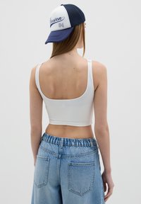 White crop top with thin straps, paired with high-waisted blue denim shorts featuring an elastic waistband and two back pockets.