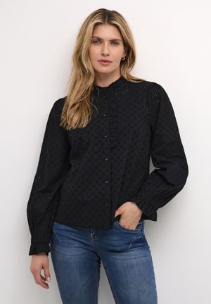 Svart knappad skjorta med volangkrage, långa puffärmar och strukturerat mönster. Matchas med ljusblå jeans.