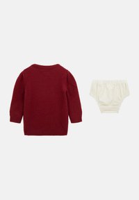 Maglione rosso lavorato a maglia con maniche lunghe e scollatura tonda, abbinato a pantaloni corti in cotone crema con elastico in vita e alle gambe.